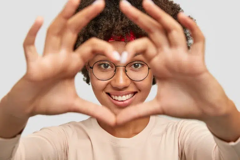 A smiling young woman making a heart emoji with her hands in front of her face